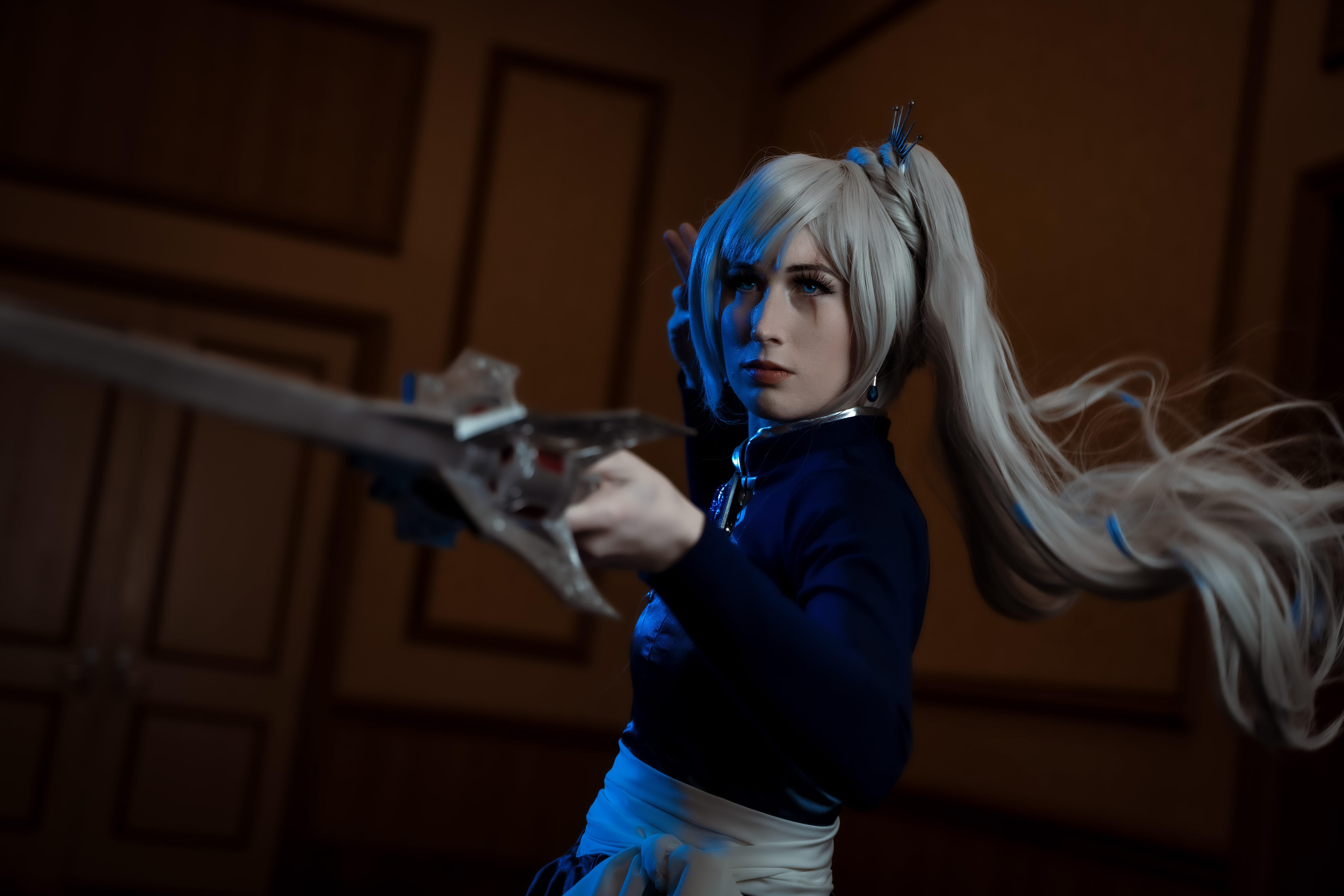 Female character with silver/white ponytail and tiara, dressed in a blue ombre dress and bolero with large silver snowflake on back. Waist is wrapped in white fabric belt and she carries a silver sword.