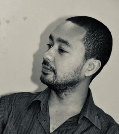 a photo of the artist, a man of Vietnamese-Djiboutian descent, with very short hair and a beard, looking thoughtfully to the side.