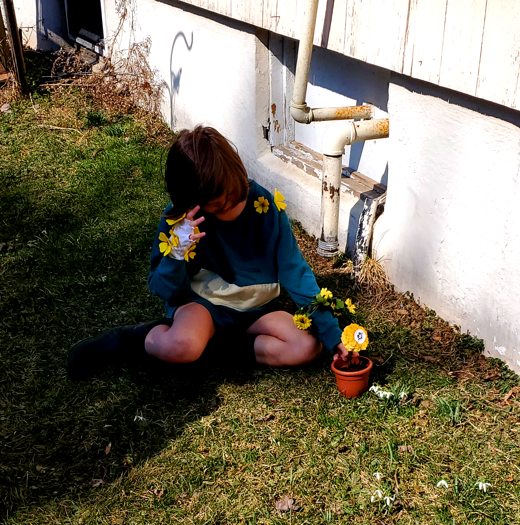 A small white child with brown hair, a green shirt with one yellow stripe, brown shorts and brown boots with an ominous smile.