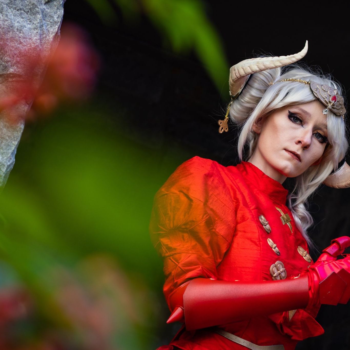Woman with horns in a red cape and tunic in front of an old building.