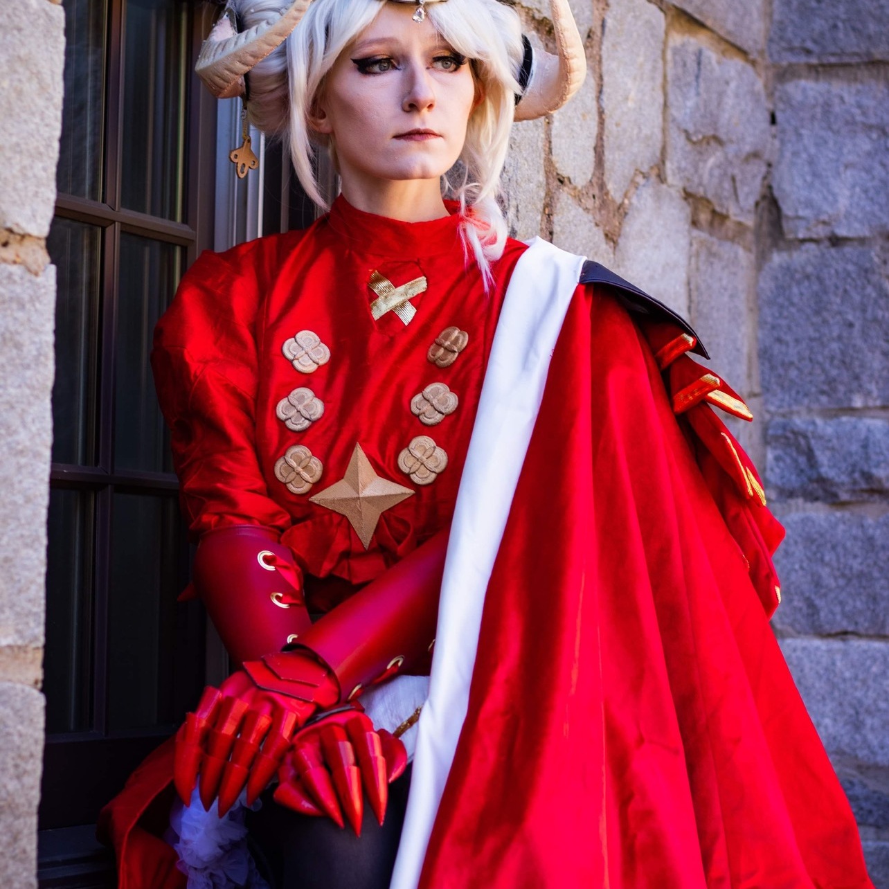 Woman with horns in a red cape and tunic in front of an old building.